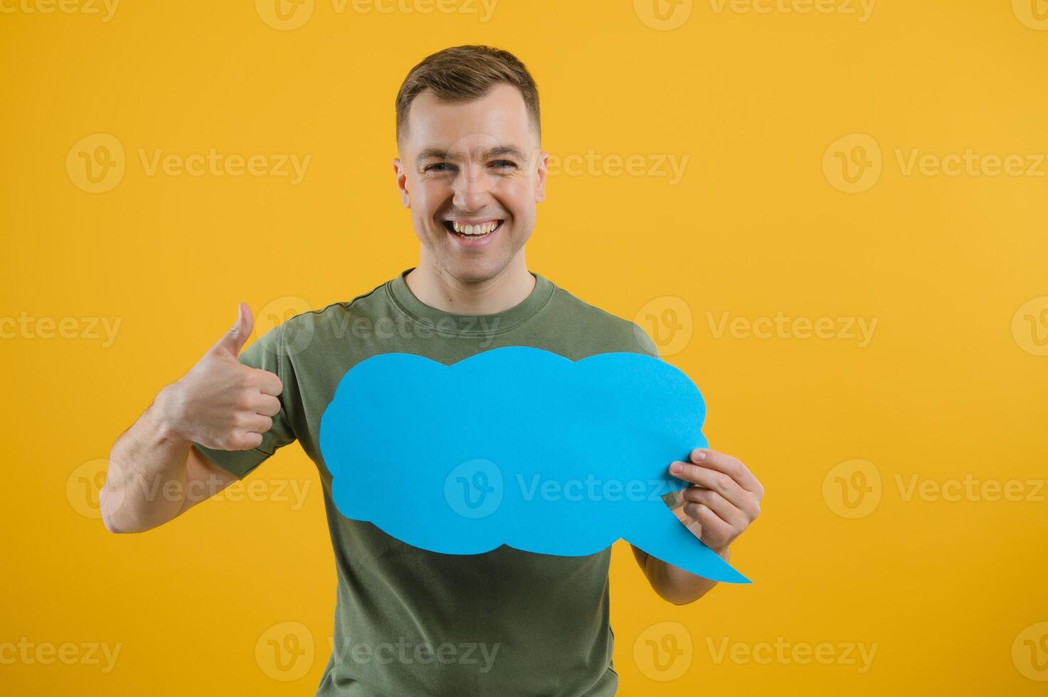 Happy guy smiling and holding blank speech balloon near head against yellow background photo