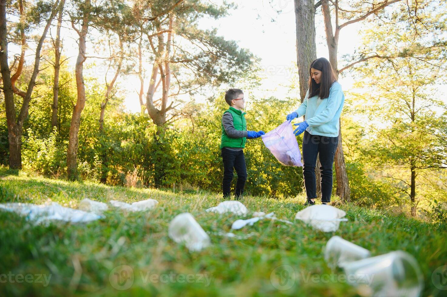 Mom teaches her son to clean up trash in nature. A woman removes plastic bottles in a bag. The topic of environmental pollution by garbage. photo
