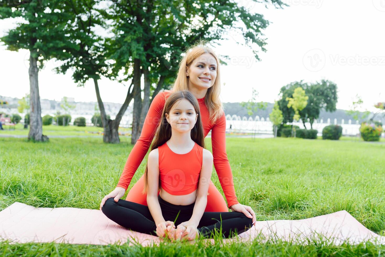 Mother and daughter doing yoga exercises on grass in the park at the day time photo