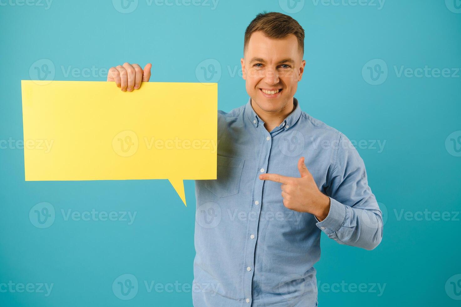 Handsome smiling man holding blank speech bubble sign isolated on light blue studio banner background with copy space photo