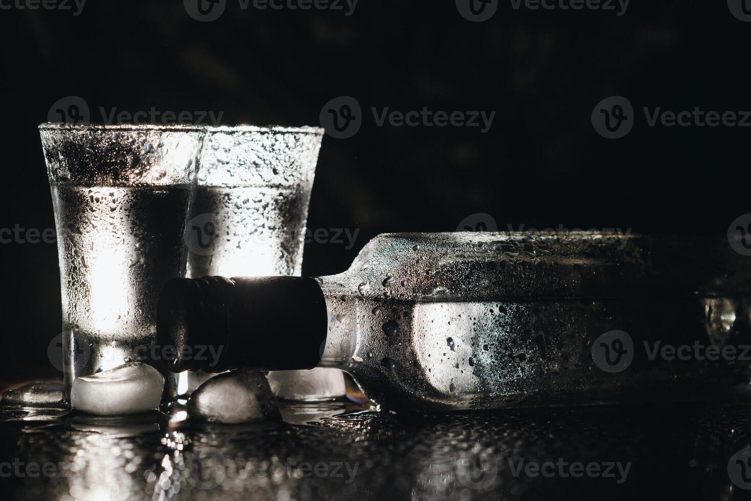 Close-up view of bottle of vodka with glasses standing on ice on black. photo