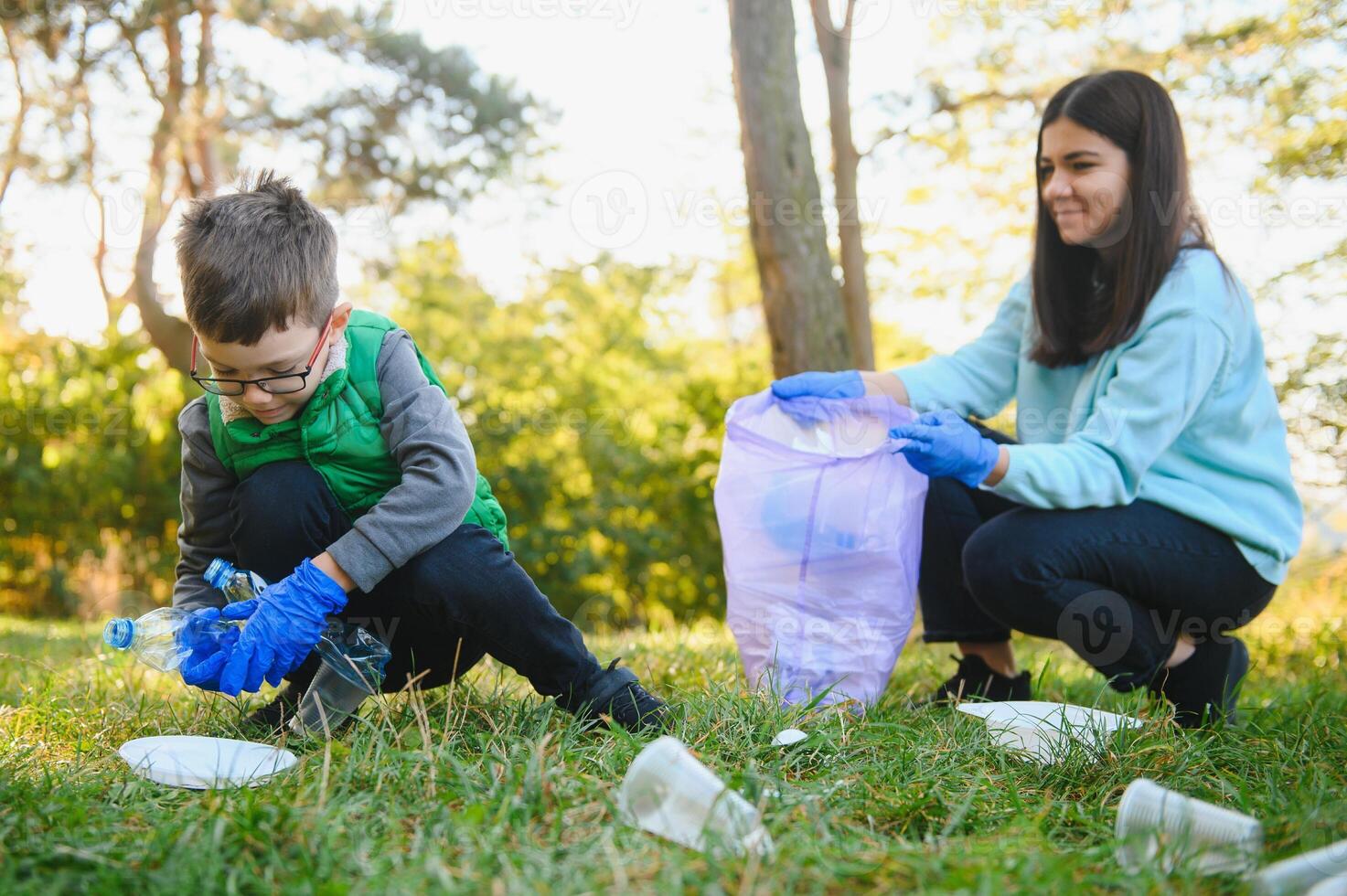 Mom teaches her son to clean up trash in nature. A woman removes plastic bottles in a bag. The topic of environmental pollution by garbage. photo