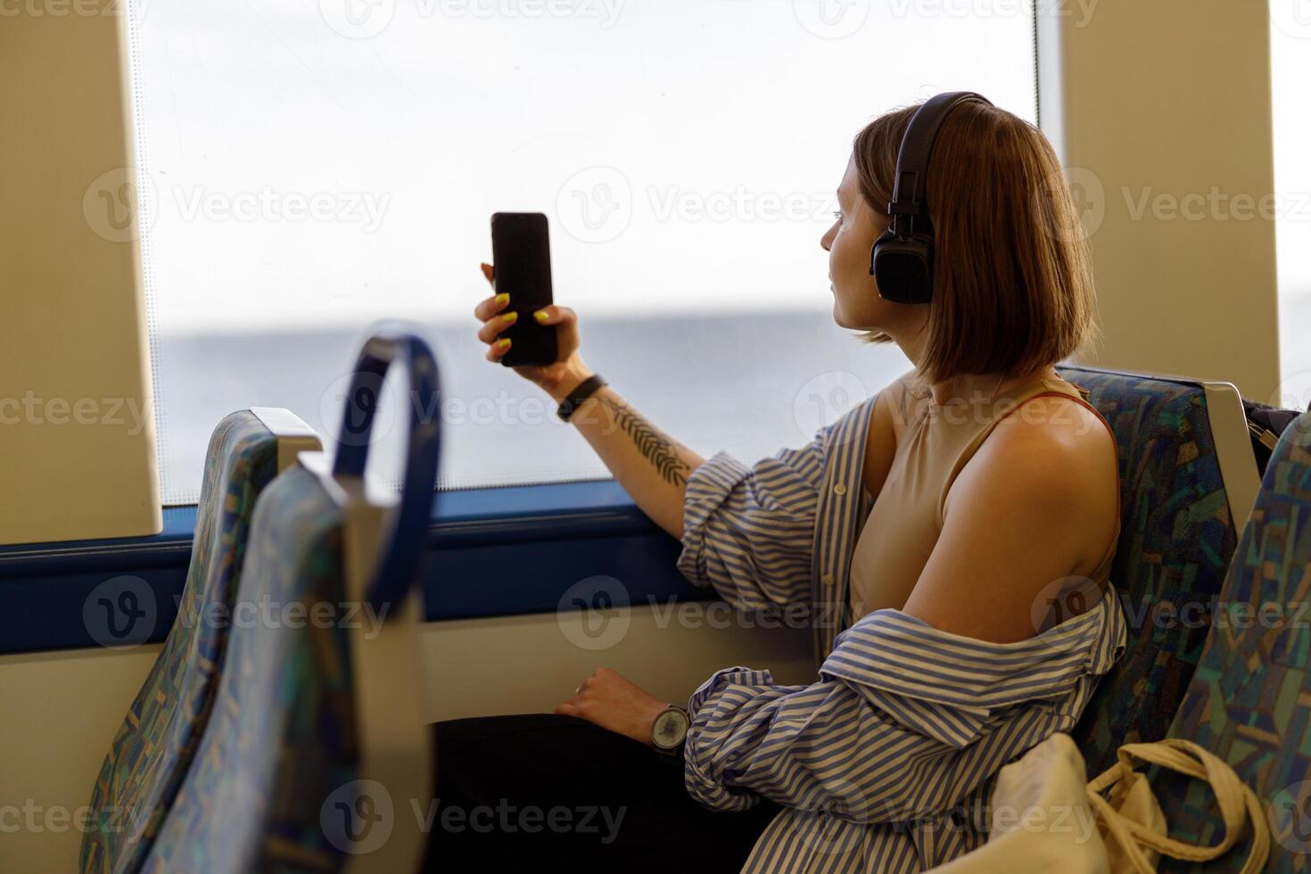 Young woman in headphones making photo on phone while traveling in public transport