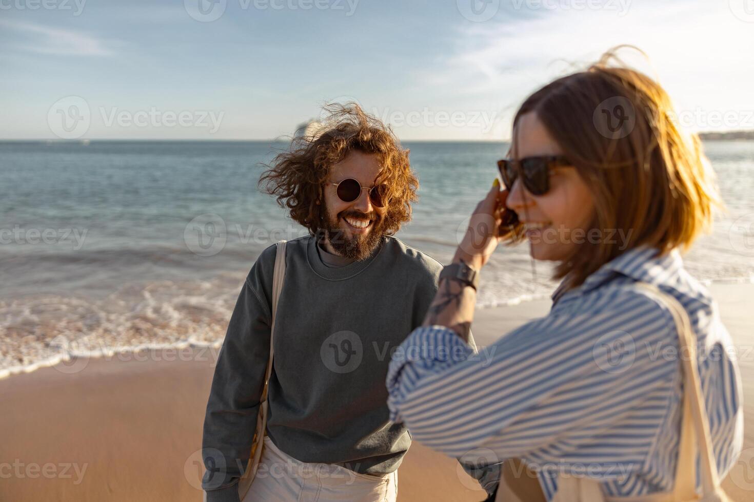 sonriendo Pareja en amor tonto alrededor mientras caminando a lo largo el playa en soleado Ventoso día foto