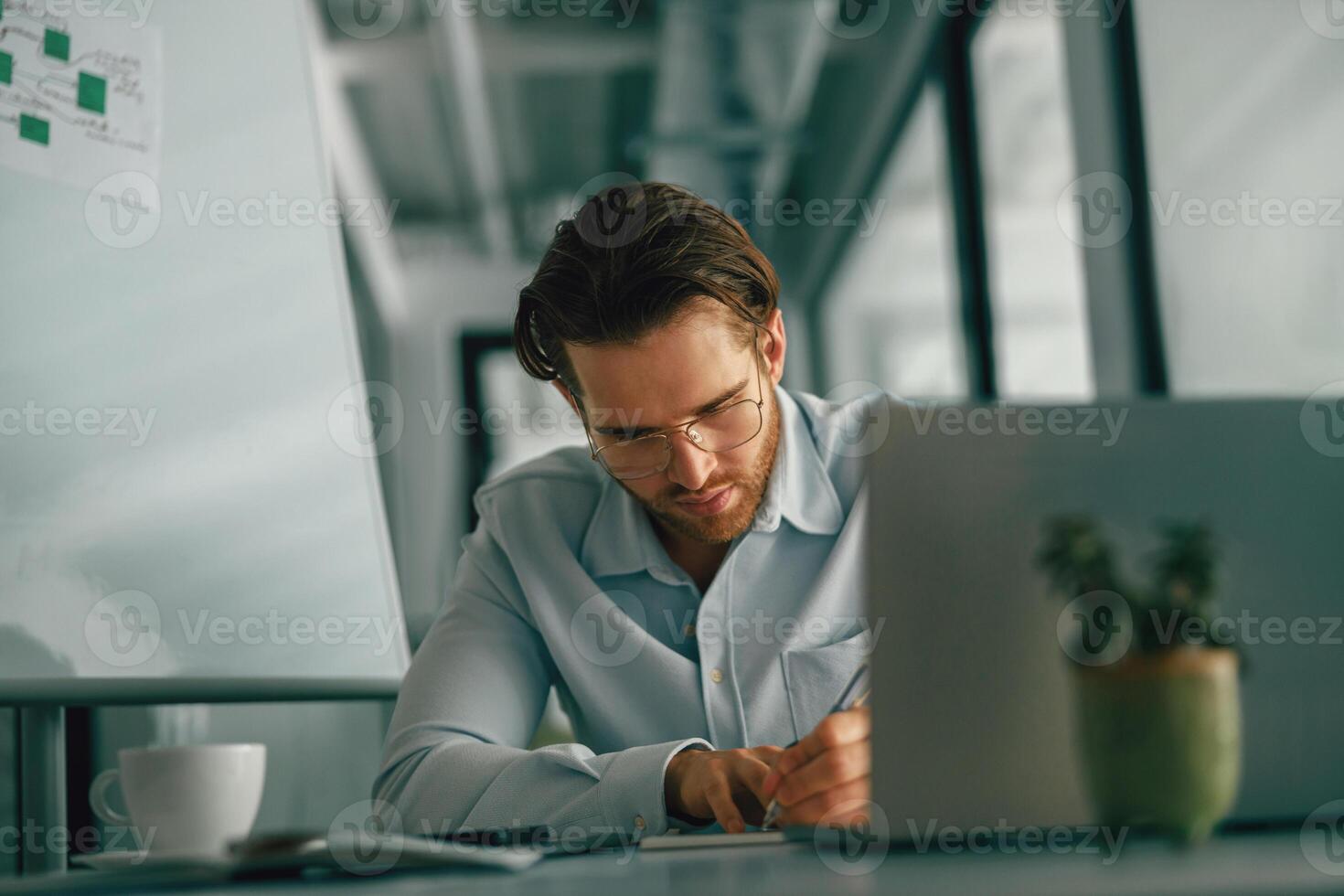 enfocado masculino persona de libre dedicación haciendo notas durante trabajando en ordenador portátil sitiing escritorio en trabajo colaborativo foto