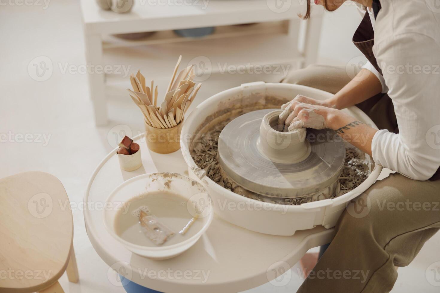 Female potter in apron making shape of clay vase on spinning pottery tool in ceramic workshop photo