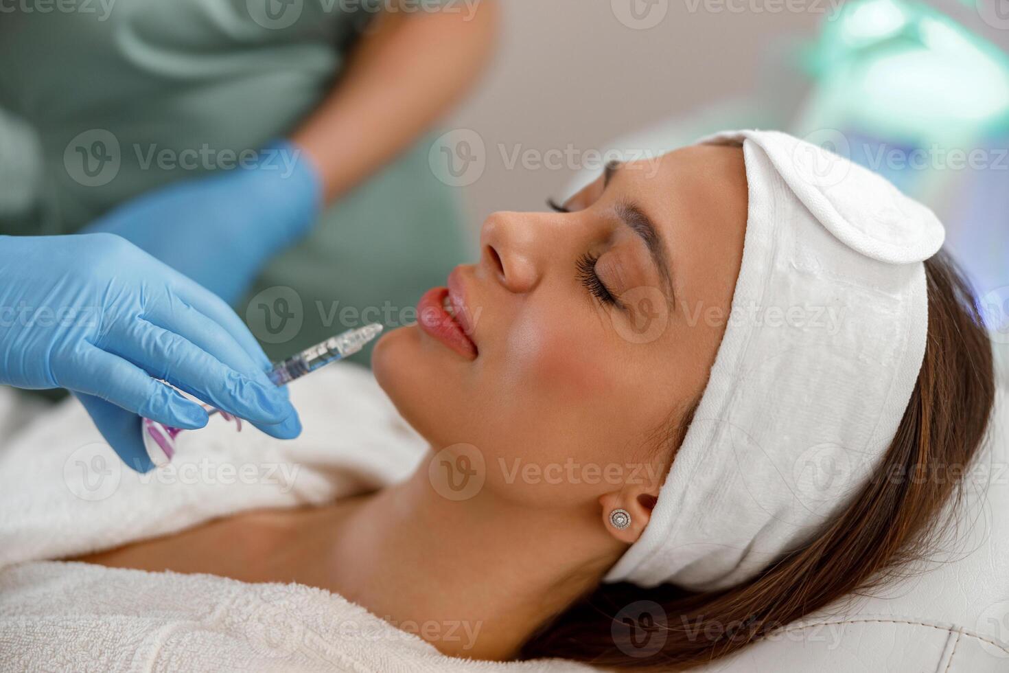 Relaxed young woman getting hyaluronic acid injections in lips at beauty salon photo