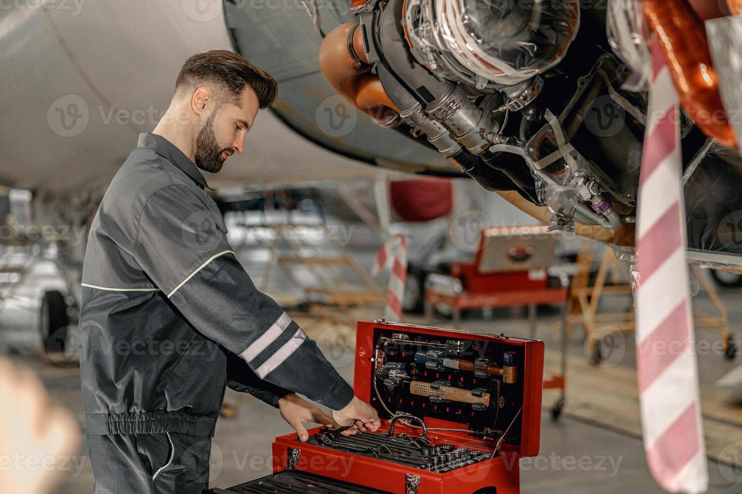 Bearded man mechanic using tool box in aircraft hangar photo