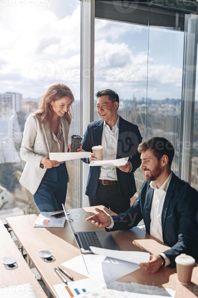 Smiling businessmen drink coffee and discussing documents with graphs and charts photo