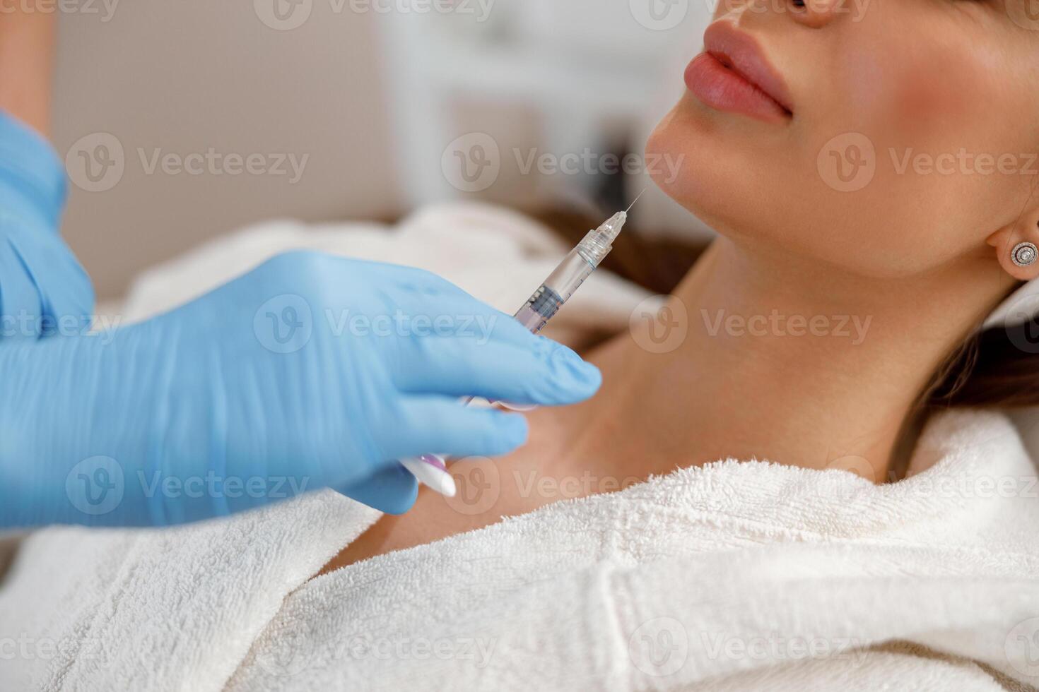 Closeup of young woman getting hyaluronic acid injections in chin at beauty salon photo