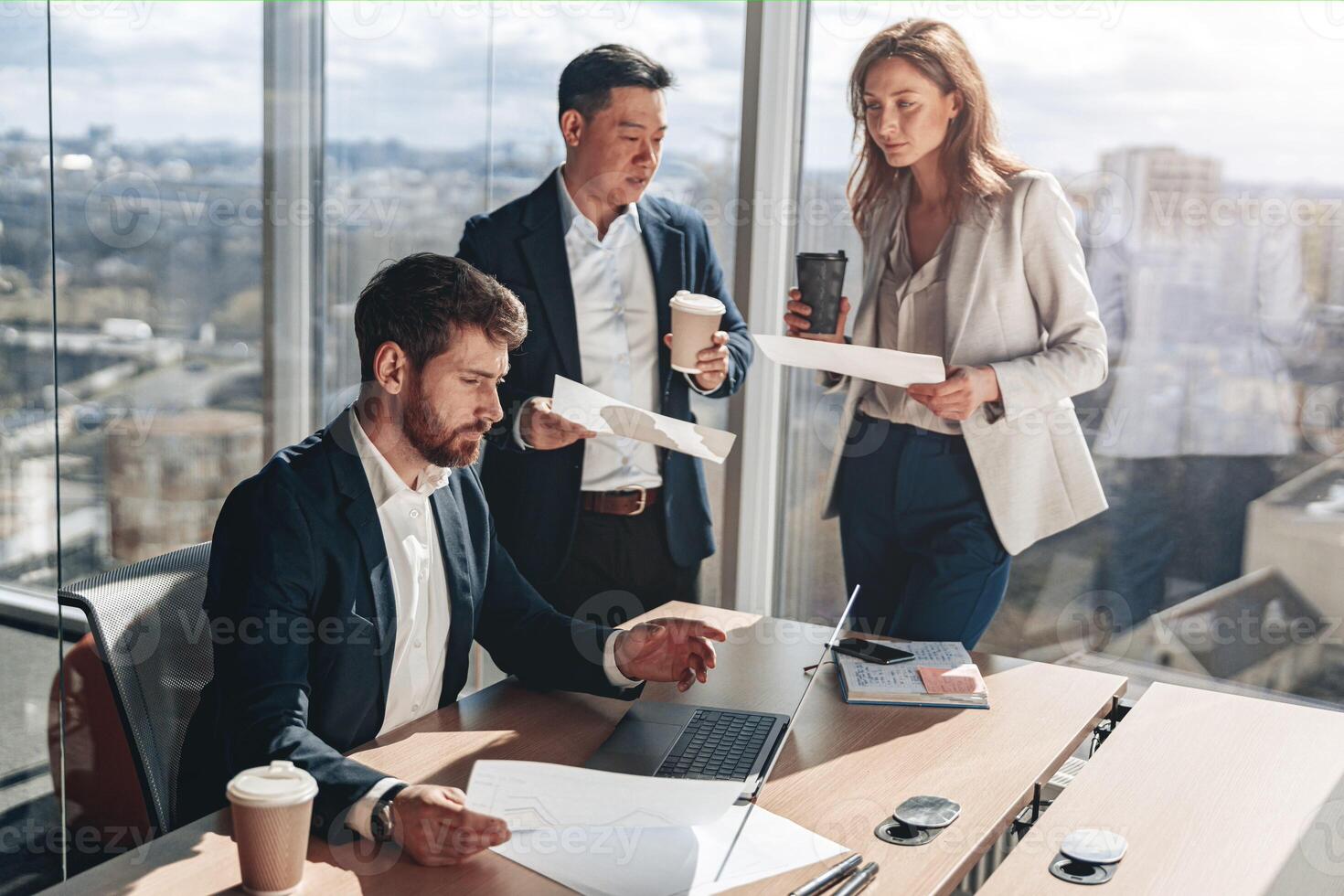 Focused businessmen drink coffee and discussing documents with graphs and charts in a modern office photo