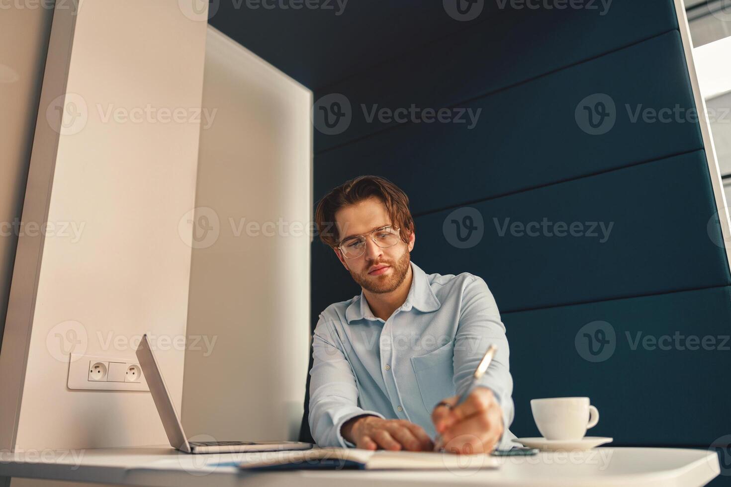 hermoso masculino persona de libre dedicación haciendo notas durante trabajando en ordenador portátil sitiing escritorio en trabajo colaborativo foto