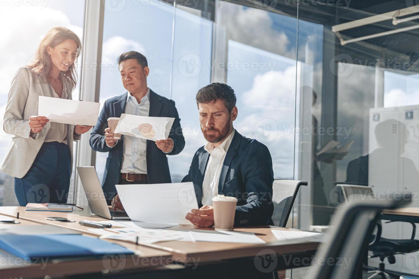 Focused businessmen discussing work issues using laptop and documents with charts photo
