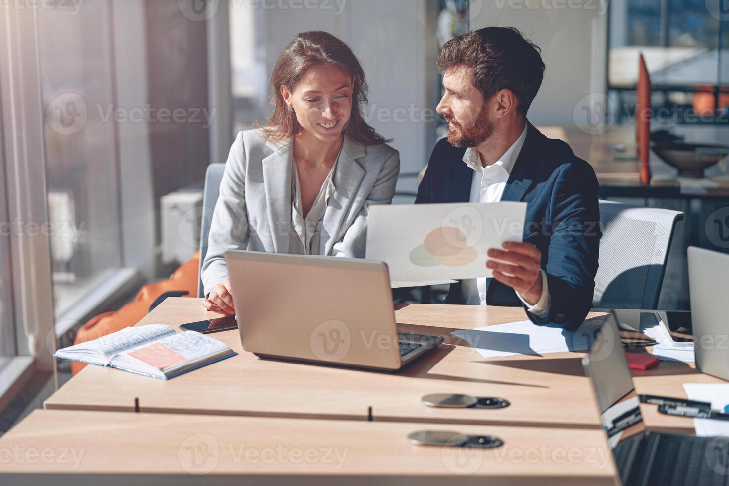 Two business people in modern office explaining statistics data to each other using laptop photo