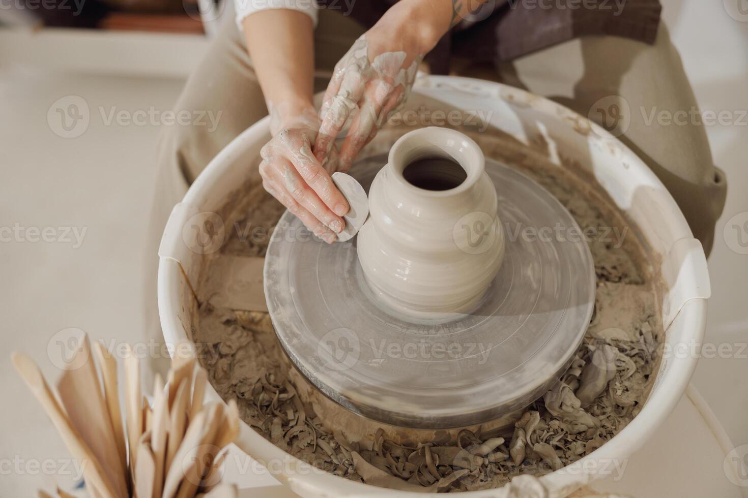 Female potter in apron making shape of clay vase on spinning pottery tool in ceramic workshop photo