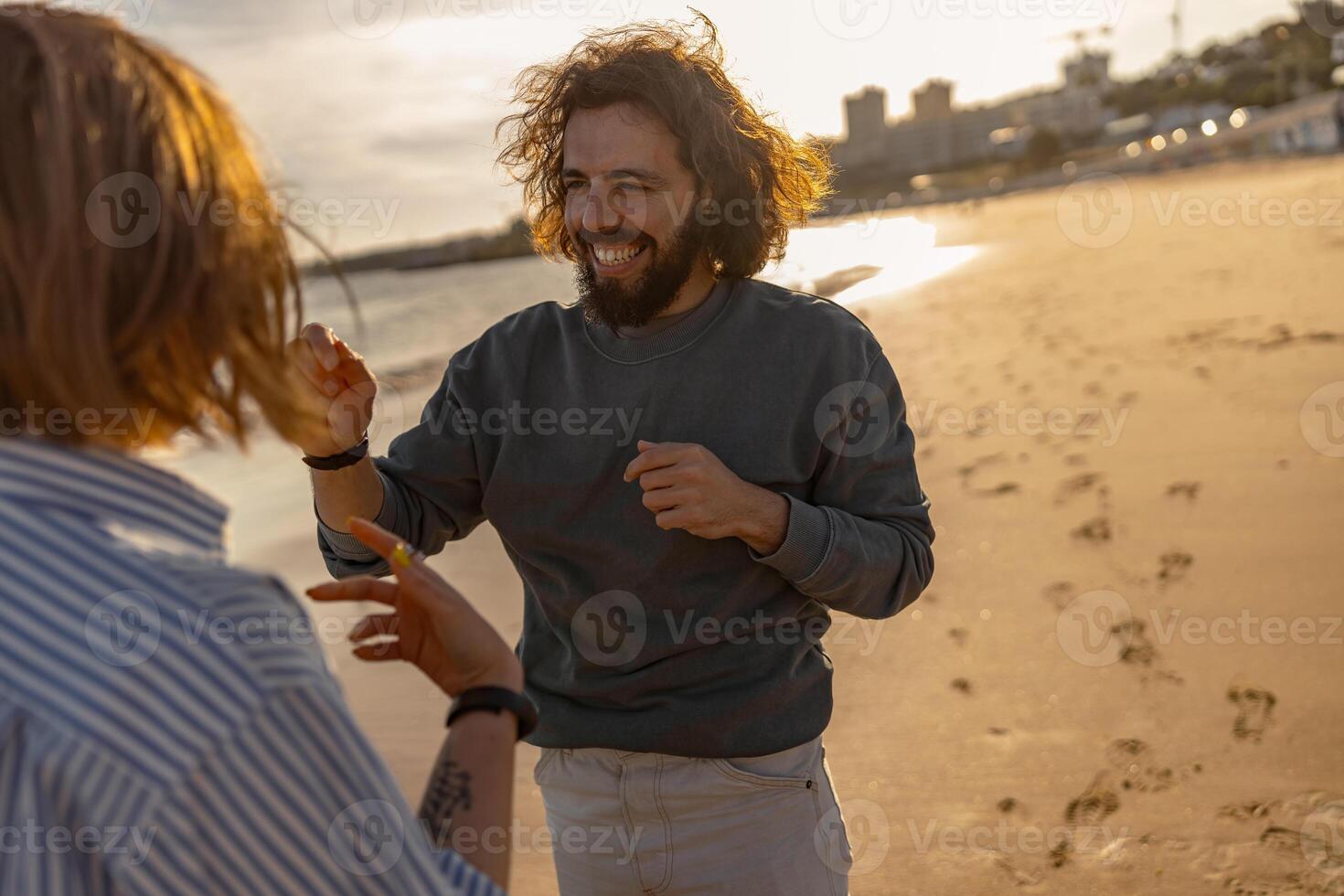 sonriendo Pareja en amor tonto alrededor mientras caminando a lo largo el playa en soleado Ventoso día foto