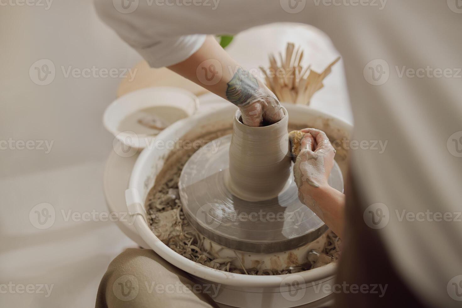 Female potter in apron making shape of clay vase on spinning pottery tool in ceramic workshop photo