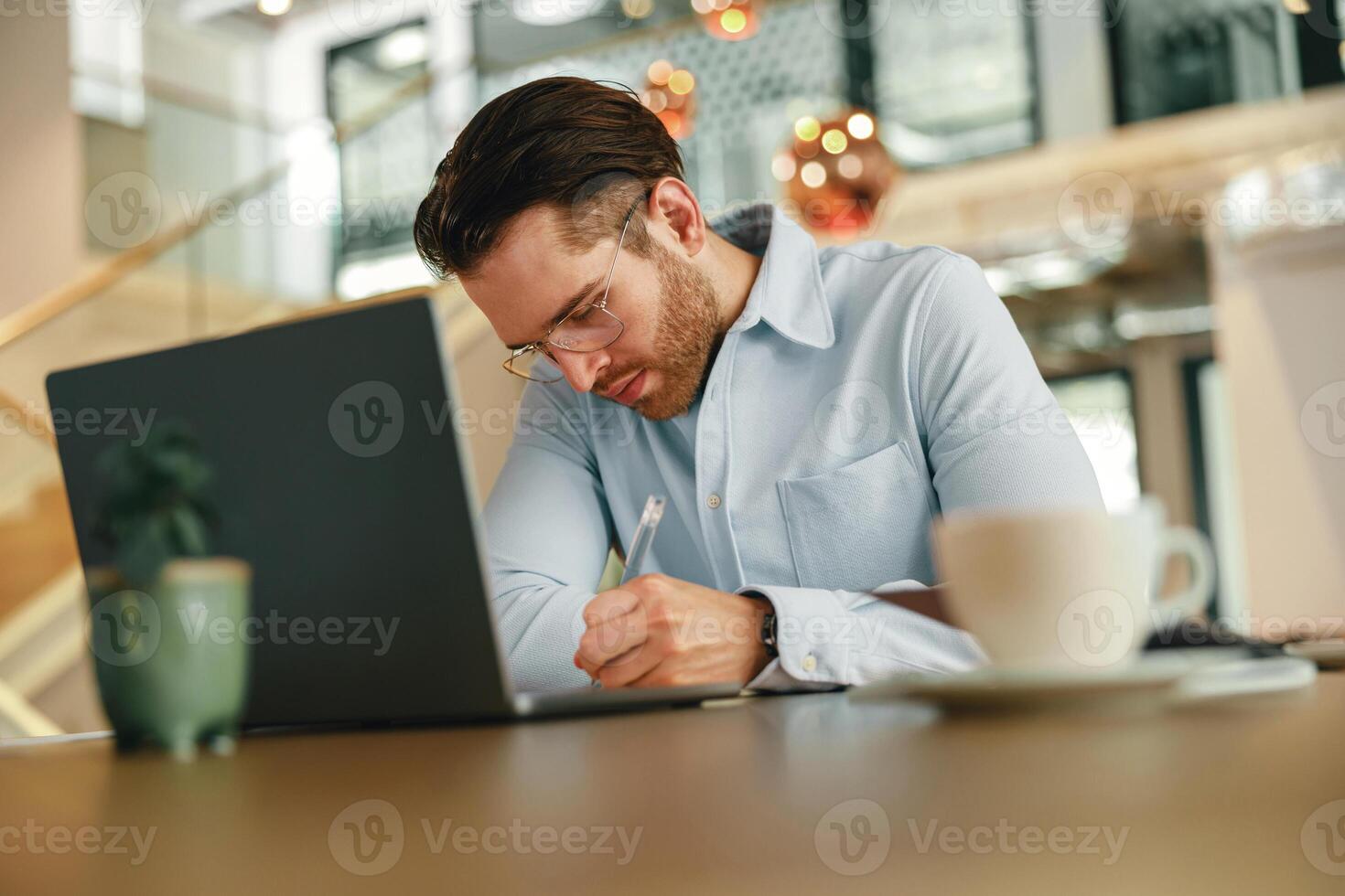 hermoso masculino persona de libre dedicación haciendo notas durante trabajando en ordenador portátil sitiing escritorio en trabajo colaborativo foto