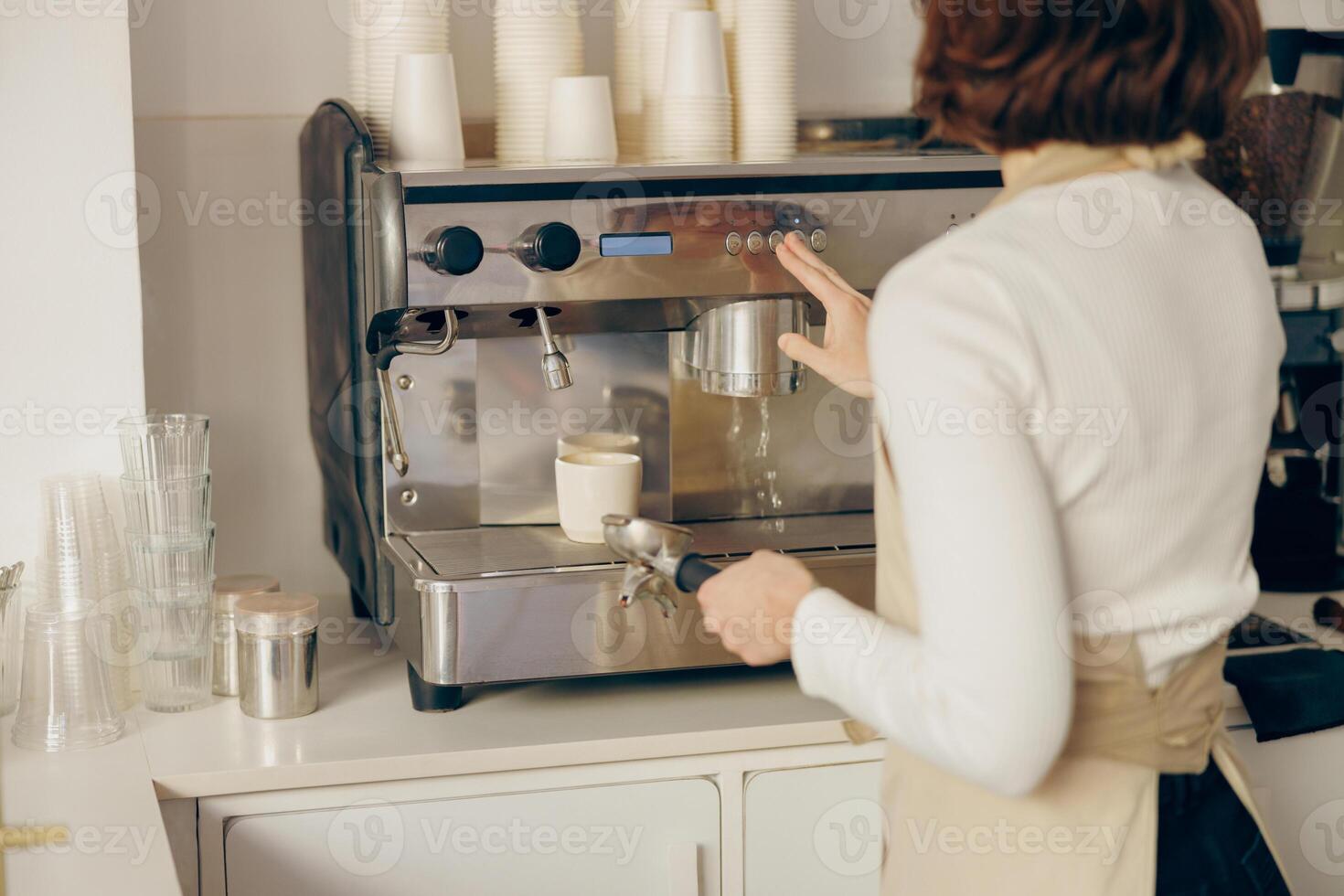 Back view of female barista making coffee in a coffee machine while working in cafe photo