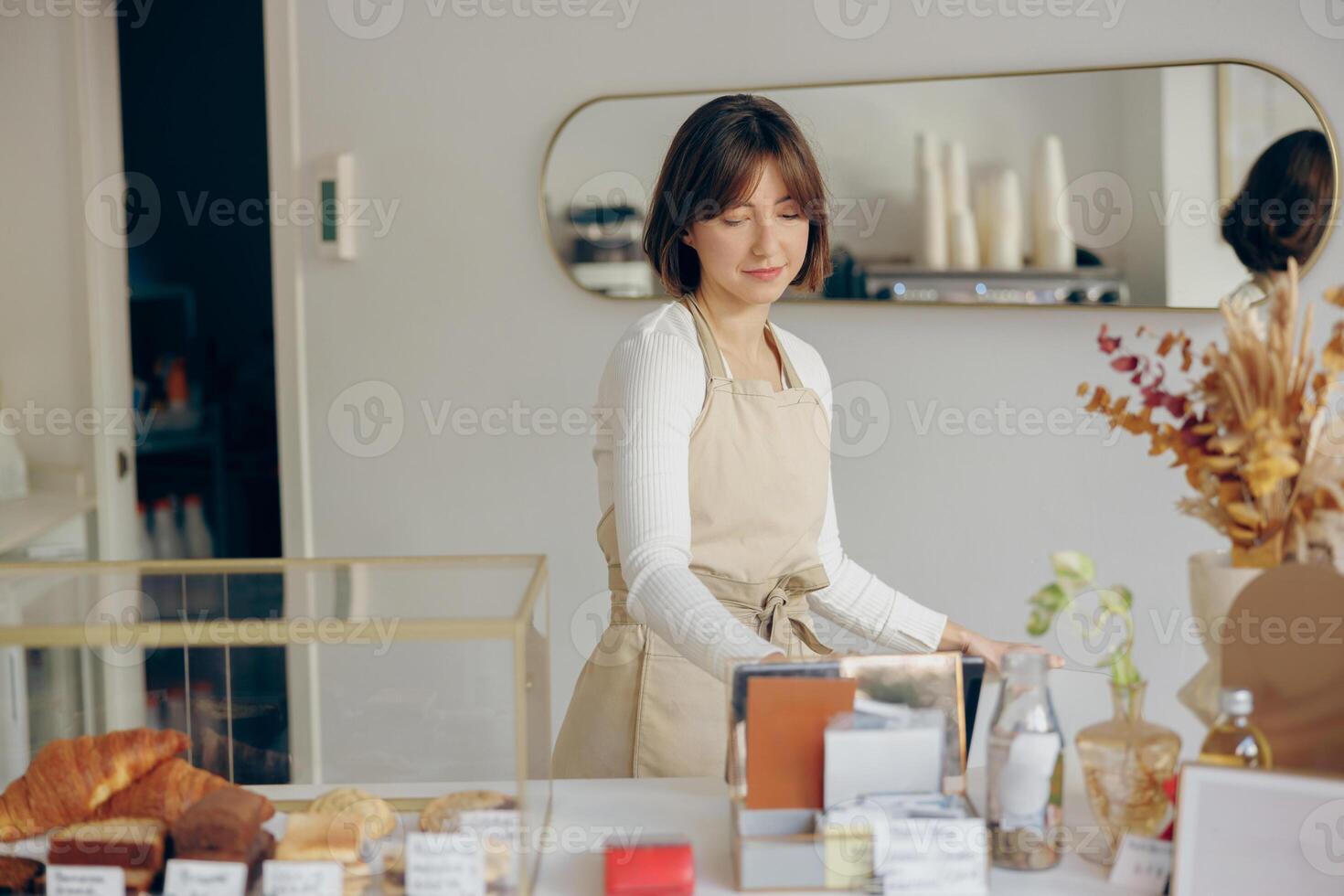 Female barista in apron standing at the counter in coffee shop and takes orders from client photo