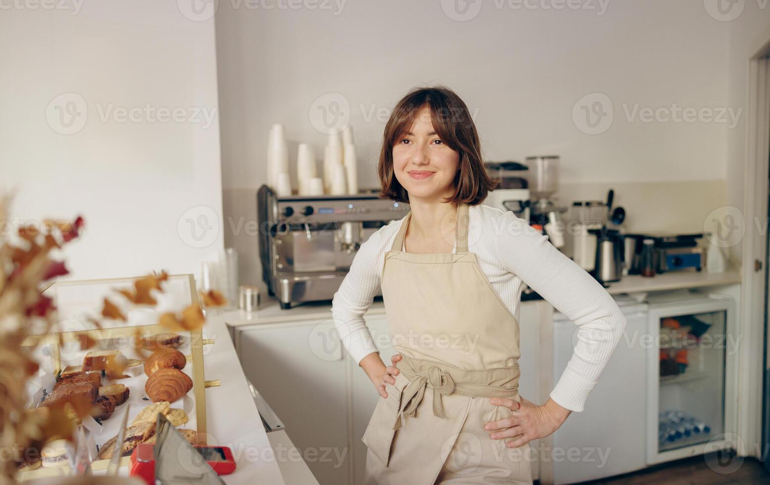 Beautiful female barista is looking at camera and smiling while standing near bar counter in cafe photo