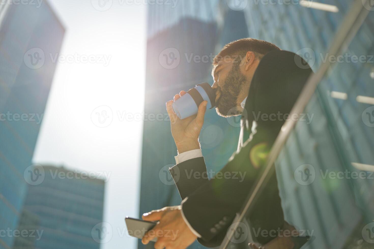 fondo ver de masculino gerente con teléfono es Bebiendo café en pie en antecedentes de ciudad rascacielos foto