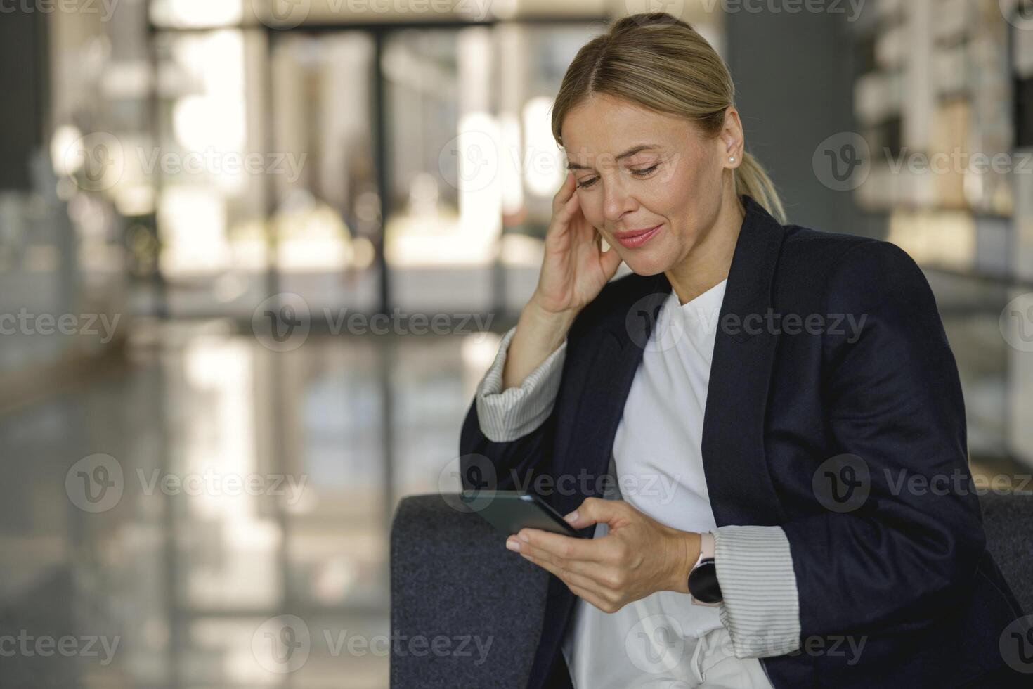 Focused female entrepreneur use phone sitting on modern office background photo