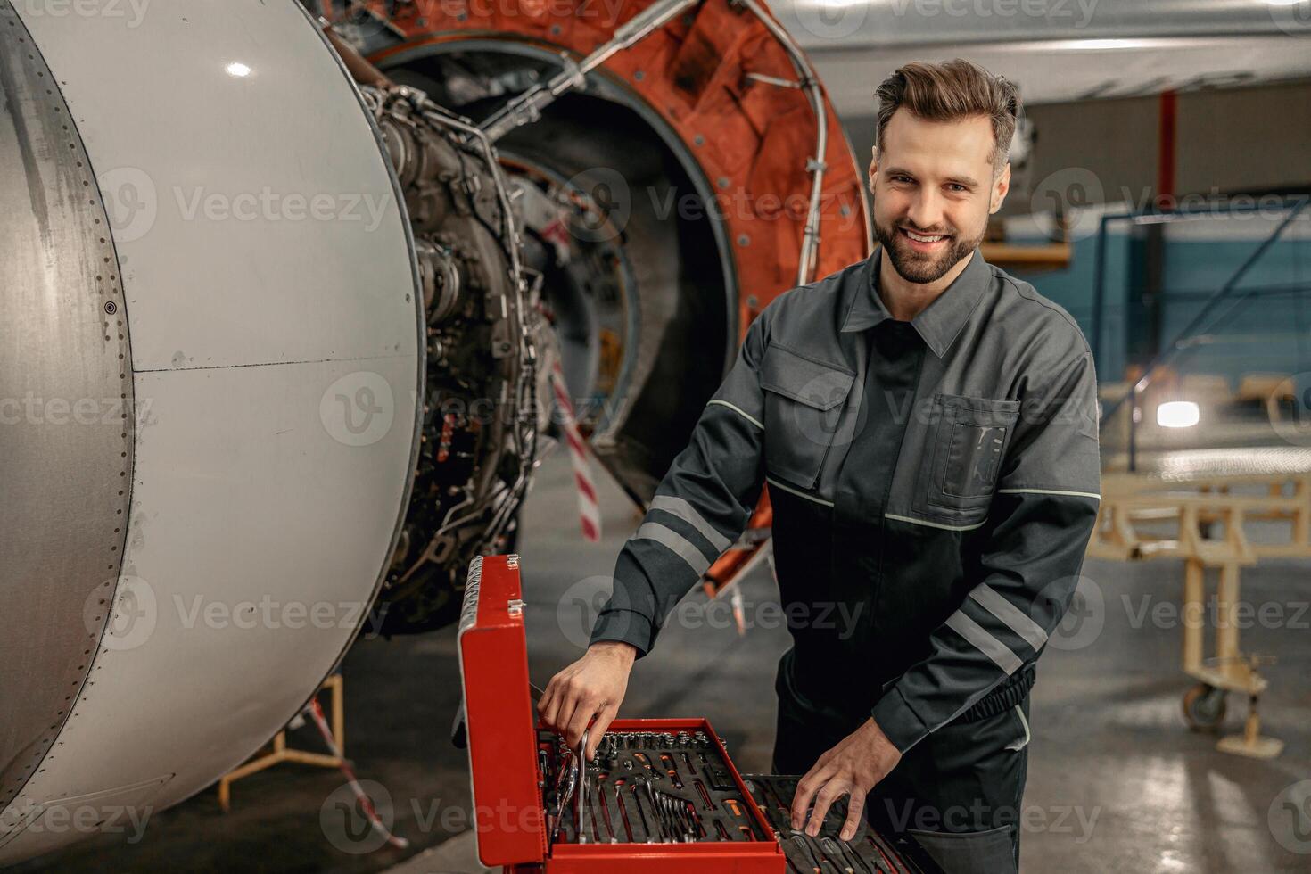 Cheerful man aircraft mechanic using tool box in hangar photo