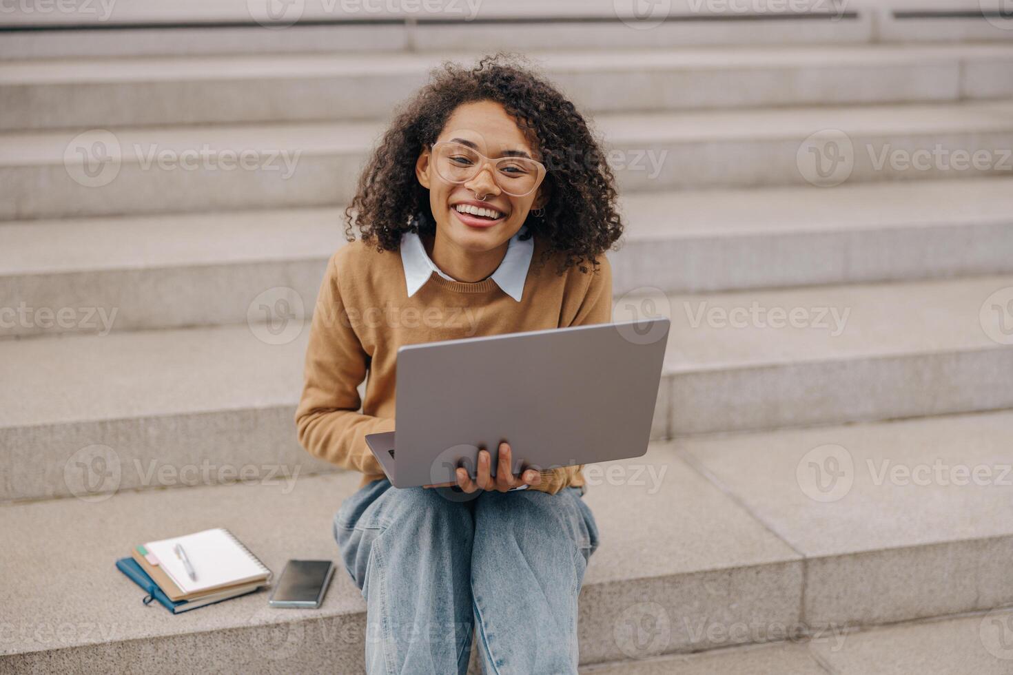 sonriente mujer gerente trabajando ordenador portátil sentado en escalera en moderno edificio antecedentes foto