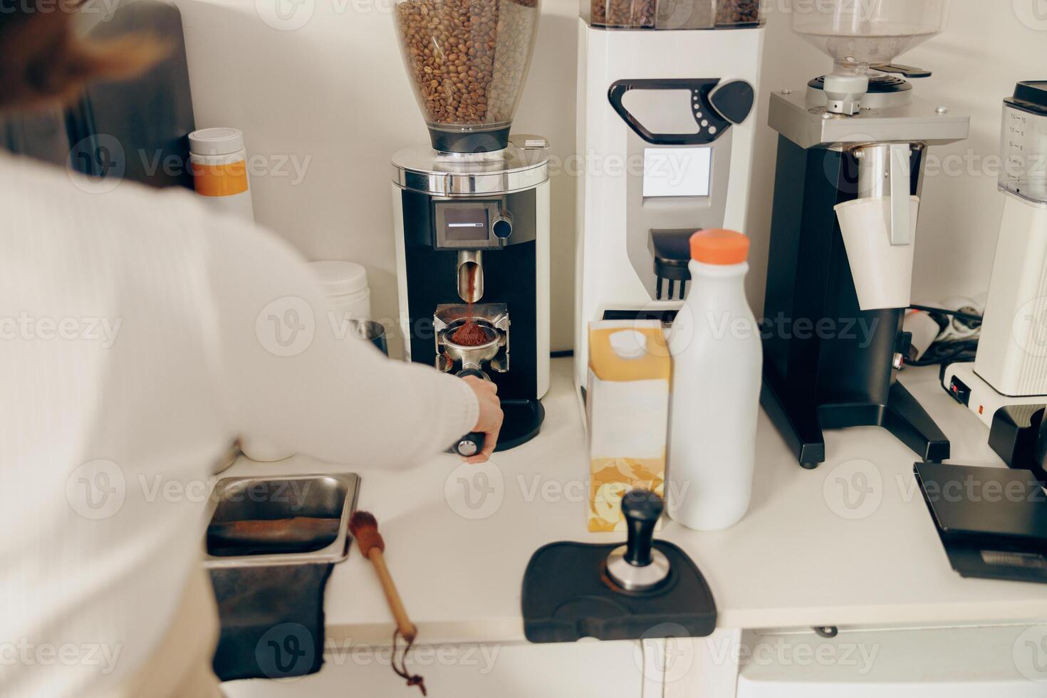 Close up of female barista grind coffee bean with grinder machine while working in cafe photo