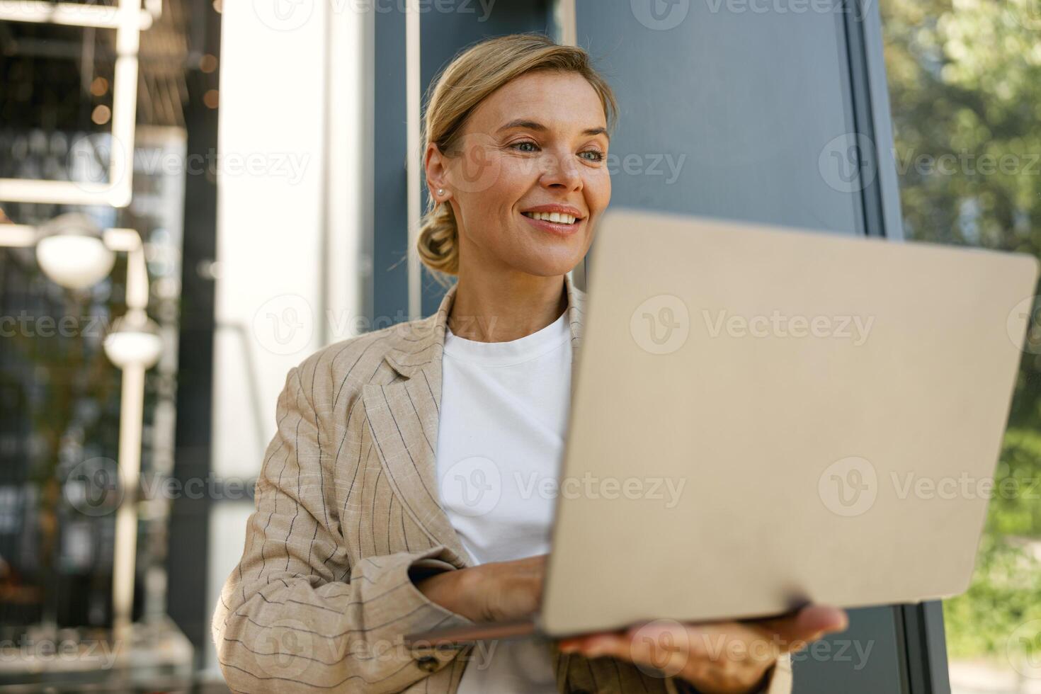 Smiling focused woman freelancer working laptop on modern building background and looks away photo