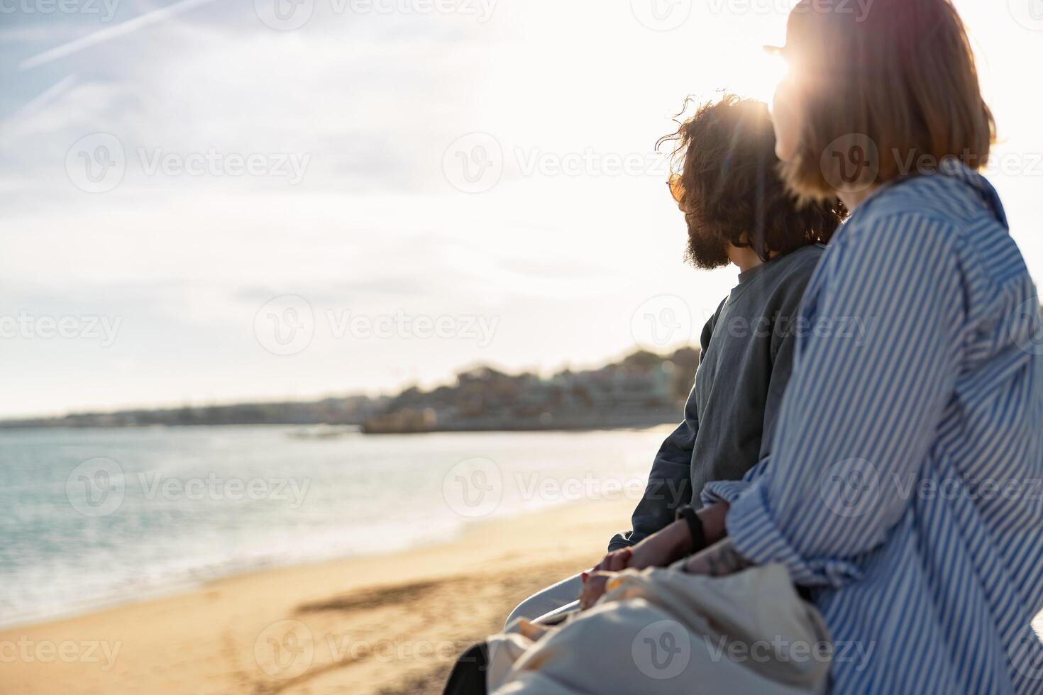 hermosa romántico Pareja sentado a el playa vistiendo casual ropa y mirando a el Oceano foto