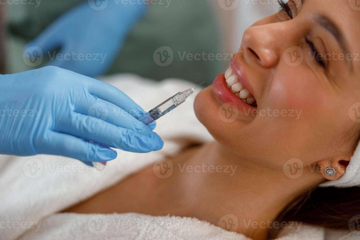 Smiling young woman getting hyaluronic acid injections in lips at beauty salon photo