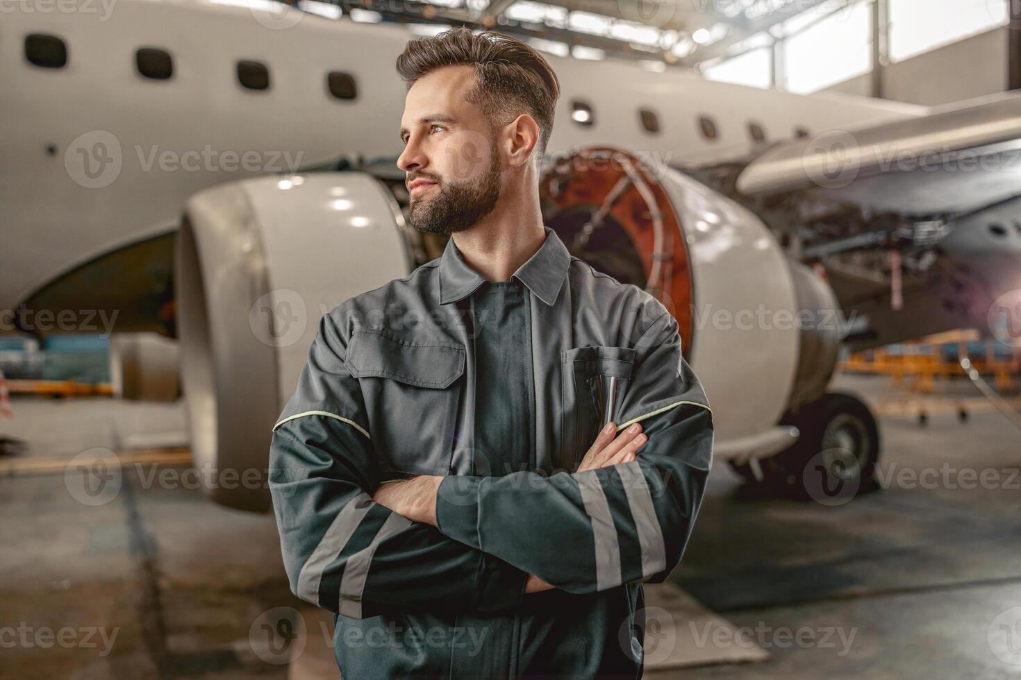 Bearded man airline mechanic standing near airplane in hangar photo