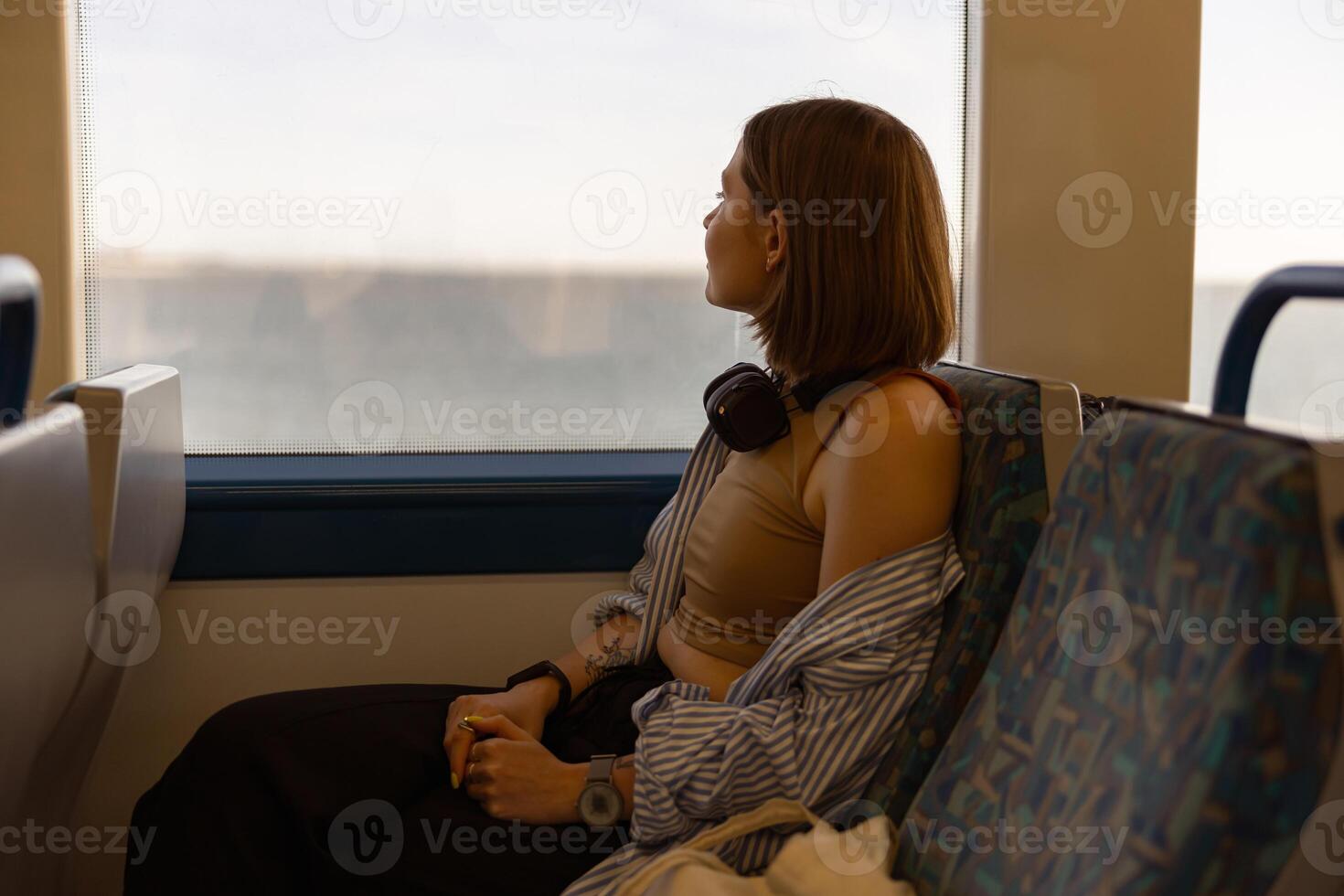 Woman in headphones while traveling in public transport and looking view outside the window photo