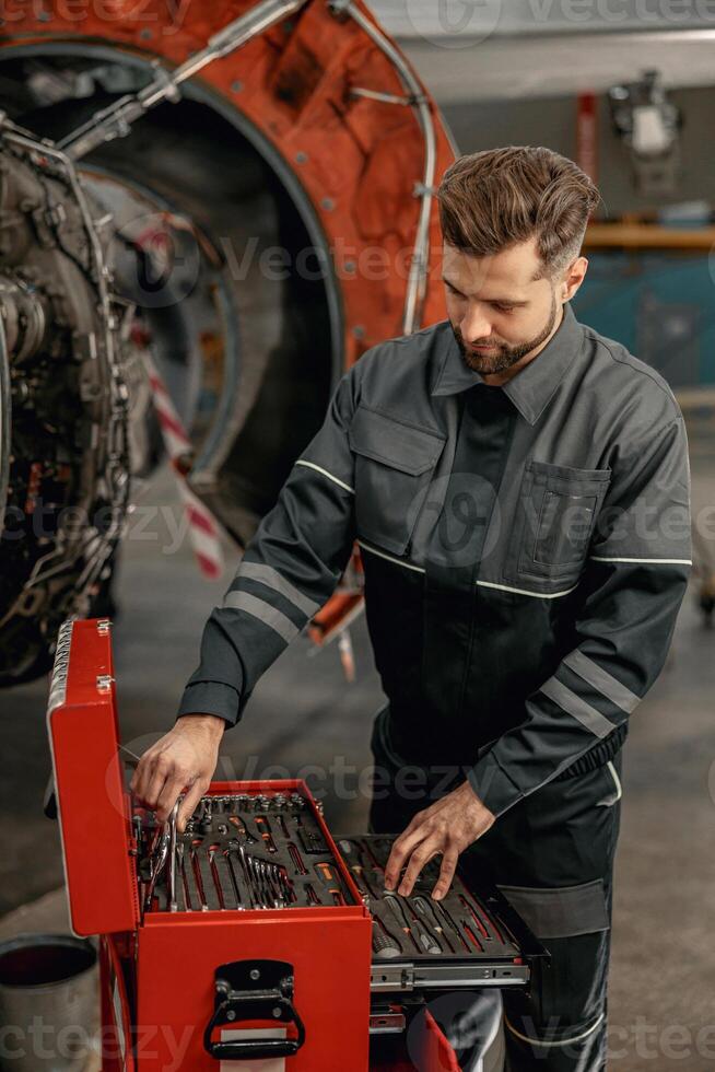 Bearded man aircraft mechanic using tool box in hangar photo