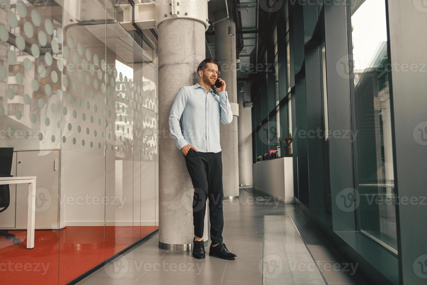 sonriente masculino ventas gerente hablando teléfono con cliente mientras en pie en trabajo colaborativo y mirando a lado foto