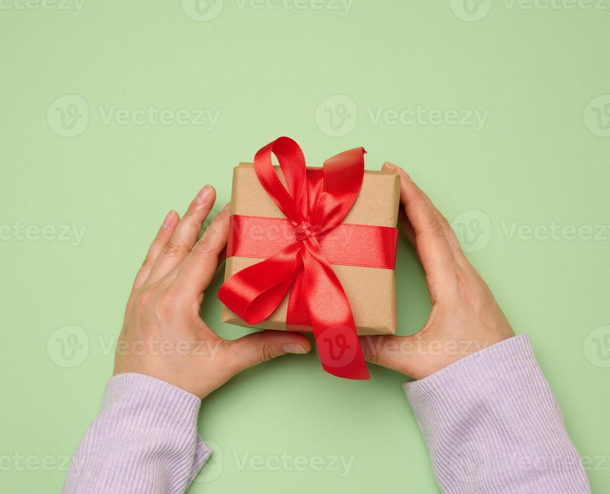 mujer mano participación un regalo caja envuelto en un rojo seda cinta en un verde antecedentes foto