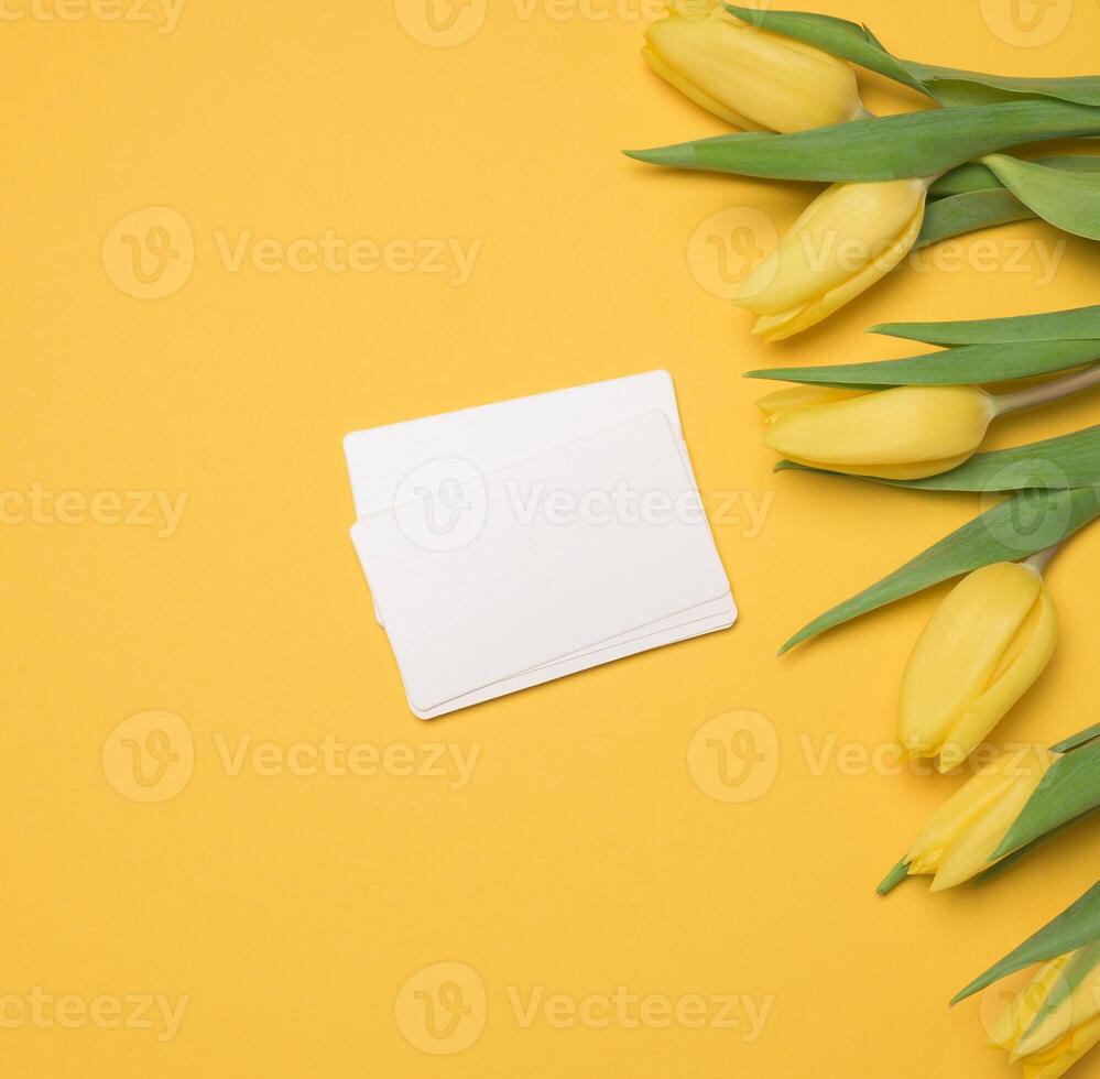blanco papel blanco negocio tarjeta y un ramo de flores de amarillo tulipanes en un amarillo antecedentes foto