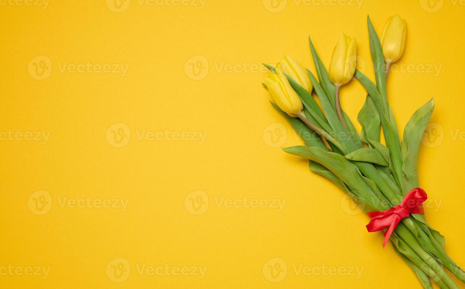 Bouquet of blooming tulips with green leaves on a yellow background, top view photo