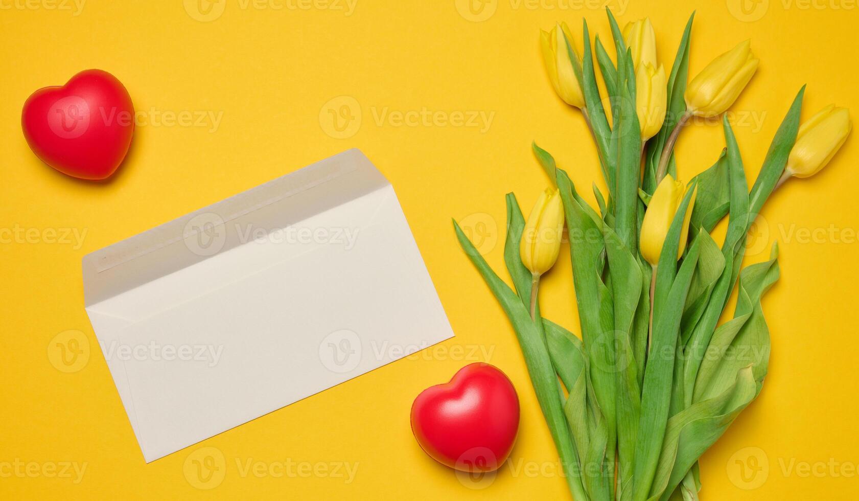 Envelope and red heart and bouquet of blooming tulips with green leaves on a yellow background photo