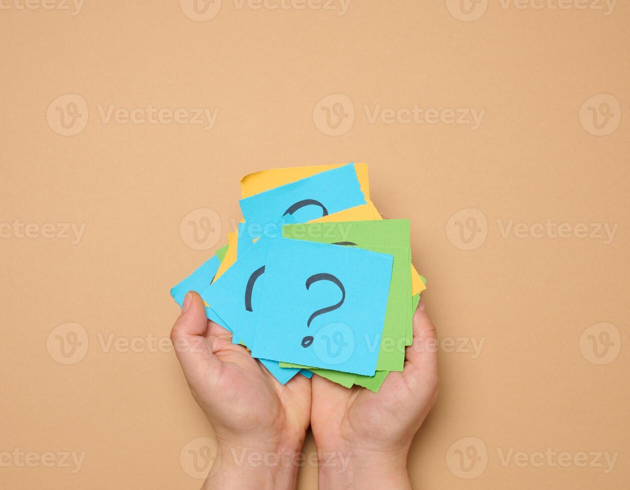 Female hands hold paper sheets with a drawn question mark on a beige background, photo