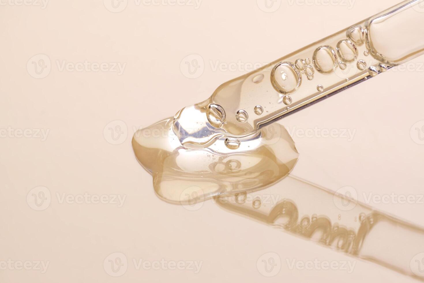 A drop of cosmetic oil falls from the pipette on beige background photo