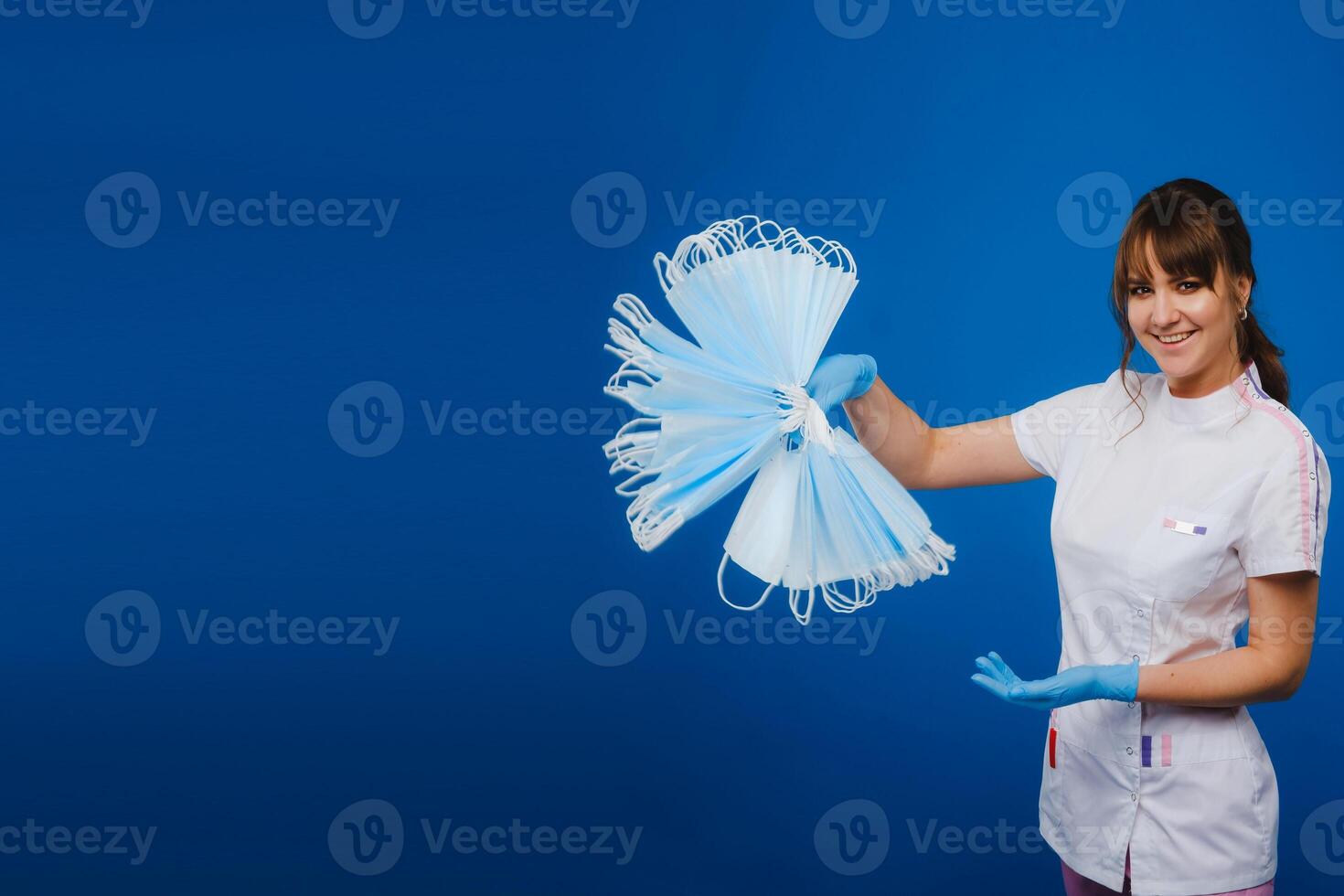 the doctor is holding a bunch of medical masks stacked together on a blue isolated background photo