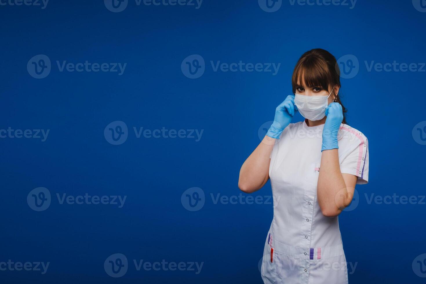A doctor girl stands in a medical mask on an isolated blue background photo