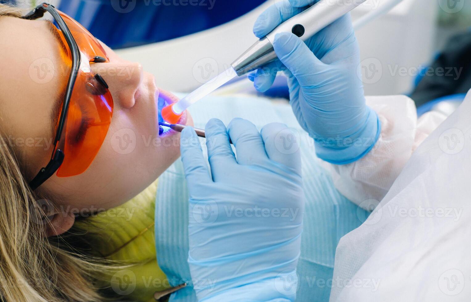 A young beautiful girl in dental glasses treats her teeth at the dentist with ultraviolet light. filling of teeth photo