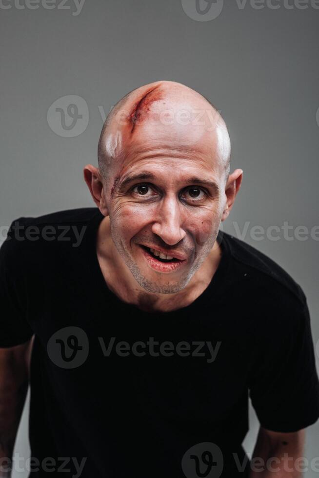 A battered man in a black T shirt who looks like a drug addict and a drunkard stands on a gray background photo