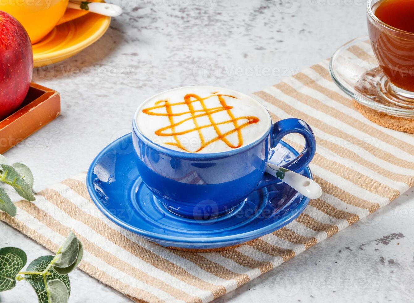 Hot caramel macchiato in blue cup on mat with grey background breakfast drink photo