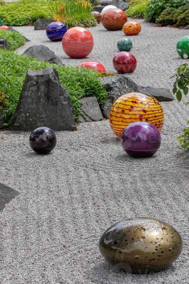 Colorful glass spheres scattered on a Zen garden's raked gravel, creating a contrast between natural tranquility and vibrant artistry at Kew Gardens, London. photo