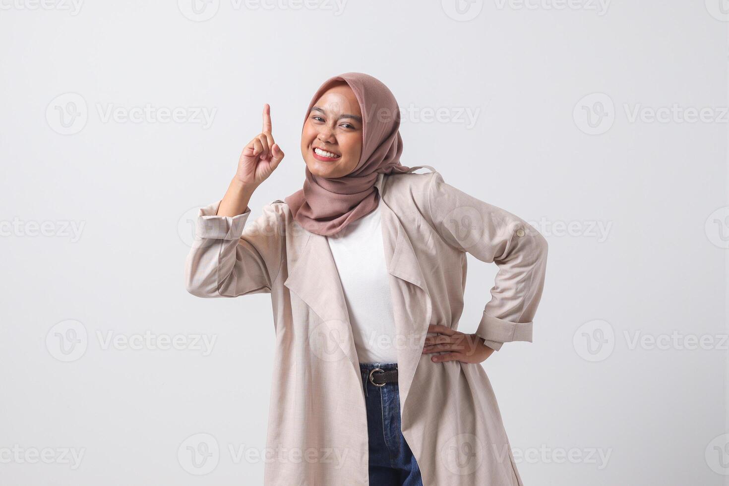 Portrait of excited Asian hijab woman in casual suit pointing up her forefinger and reminding something to do. Businesswoman concept. Isolated image on white background photo